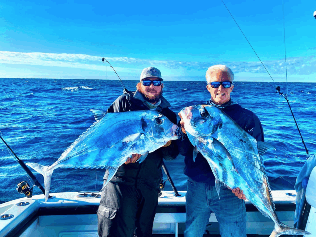 Two anglers proudly holding large African pompanos on a fishing charter in the Florida Keys, with a vibrant blue ocean and clear sky in the background.