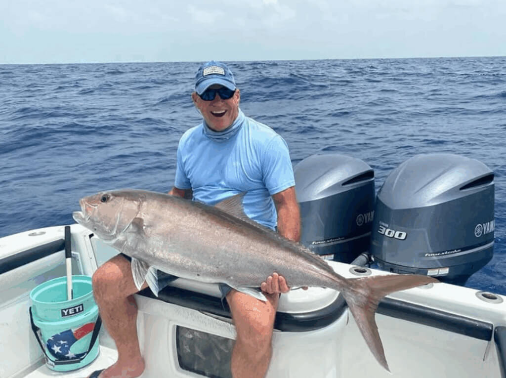 Man sitting on a boat holding a large Amberjack fish, with two Yamaha outboard motors in the background, showcasing successful offshore fishing in the Florida Keys.