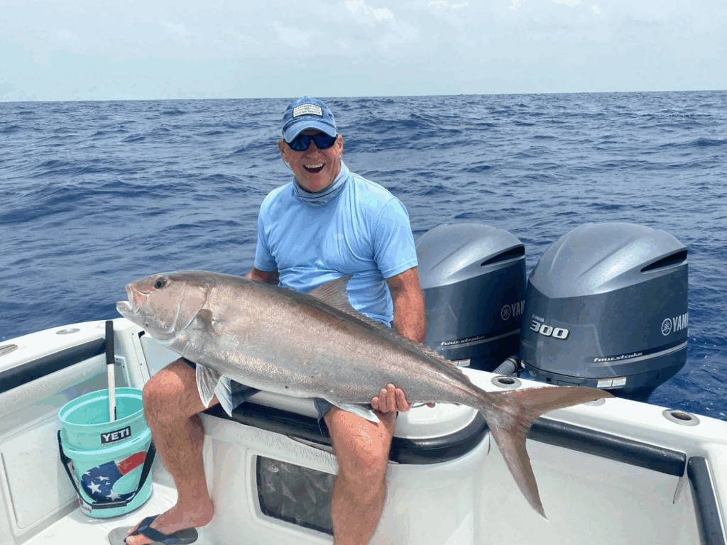 Man sitting on a boat holding a large amberjack fish, with two Yamaha outboard motors in the background, showcasing a successful catch during wreck fishing in the Florida Keys.