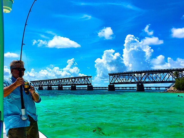 Fisherman casting a line in turquoise waters near the iconic Bahia Honda bridge in the Florida Keys, showcasing the vibrant fishing environment.