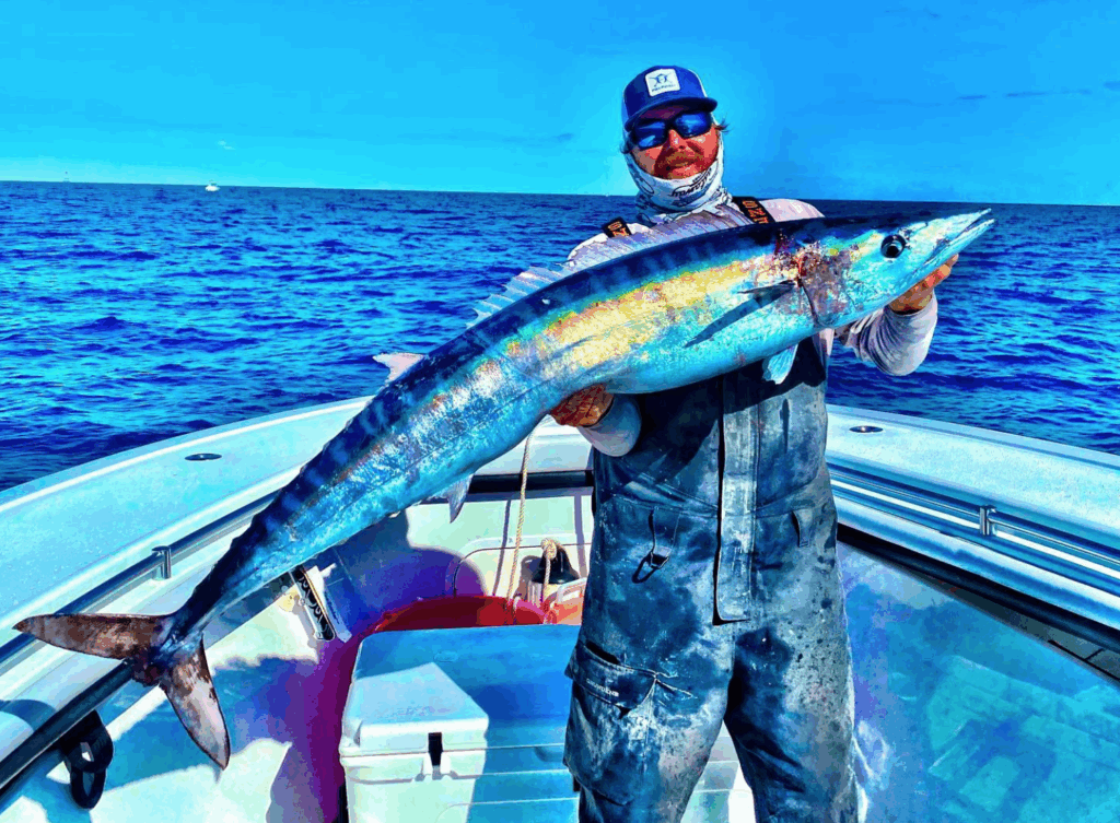 Man holding a large Wahoo fish on a boat in the Florida Keys, showcasing the excitement of offshore fishing adventures for Blackfin Tuna, Mahi Mahi, and Sailfish.