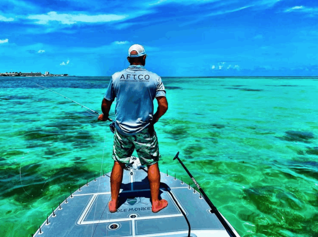 Man fishing from a boat in the clear turquoise waters of the Florida Keys, wearing an AFTCO shirt, showcasing inshore flats fishing experience.