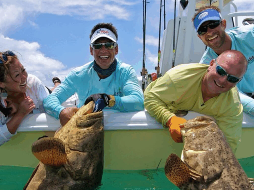 Group of anglers joyfully holding large Goliath Groupers while fishing in the Florida Keys, showcasing a successful catch during a charter trip.