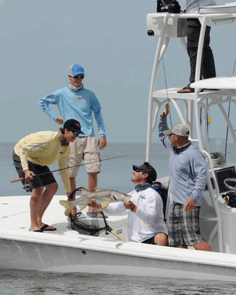 Group of anglers on a fishing boat celebrating a catch of a large Snook, showcasing the excitement of inshore flats fishing in the Florida Keys.