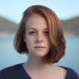 Young woman with red hair, smiling, in front of a blurred water background, reflecting the fun and adventure of fishing charters in the Florida Keys.