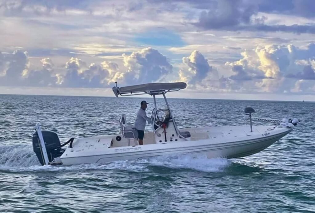 24′ bay boat navigating the waters of the Florida Keys, equipped for inshore and offshore fishing, with a captain at the helm against a backdrop of clouds and water.