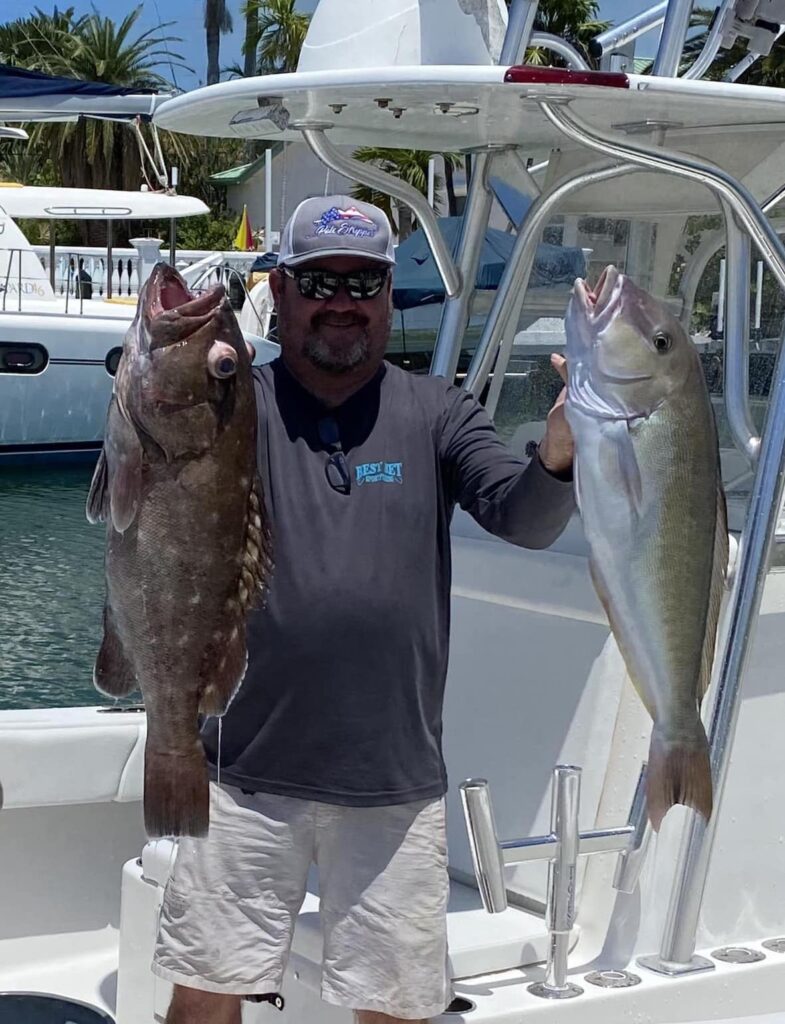 Man holding two large fish, a grouper and a snapper, on a fishing charter boat in the Florida Keys, showcasing successful catch and fishing experience.