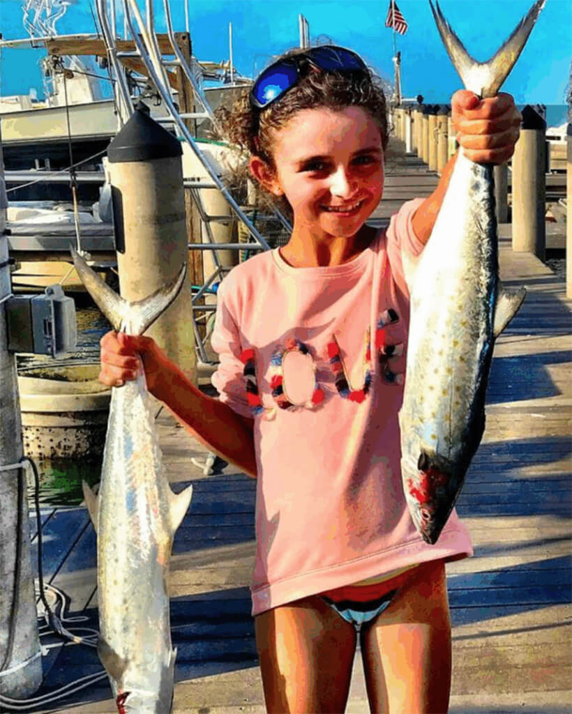 Girl holding two Spanish Mackerel on a fishing dock in the Florida Keys, showcasing a successful fishing trip.