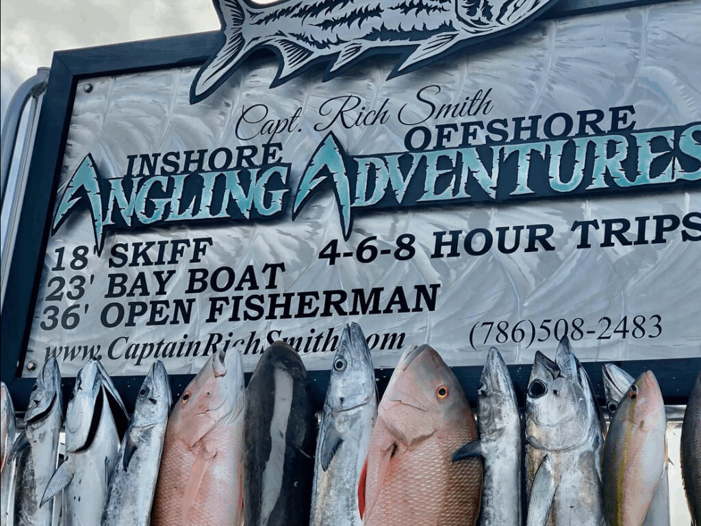 Sign showcasing Captain Rich Smith's Angling Adventures, featuring a variety of fish including snapper and tuna, with details on fishing trip options and contact information.