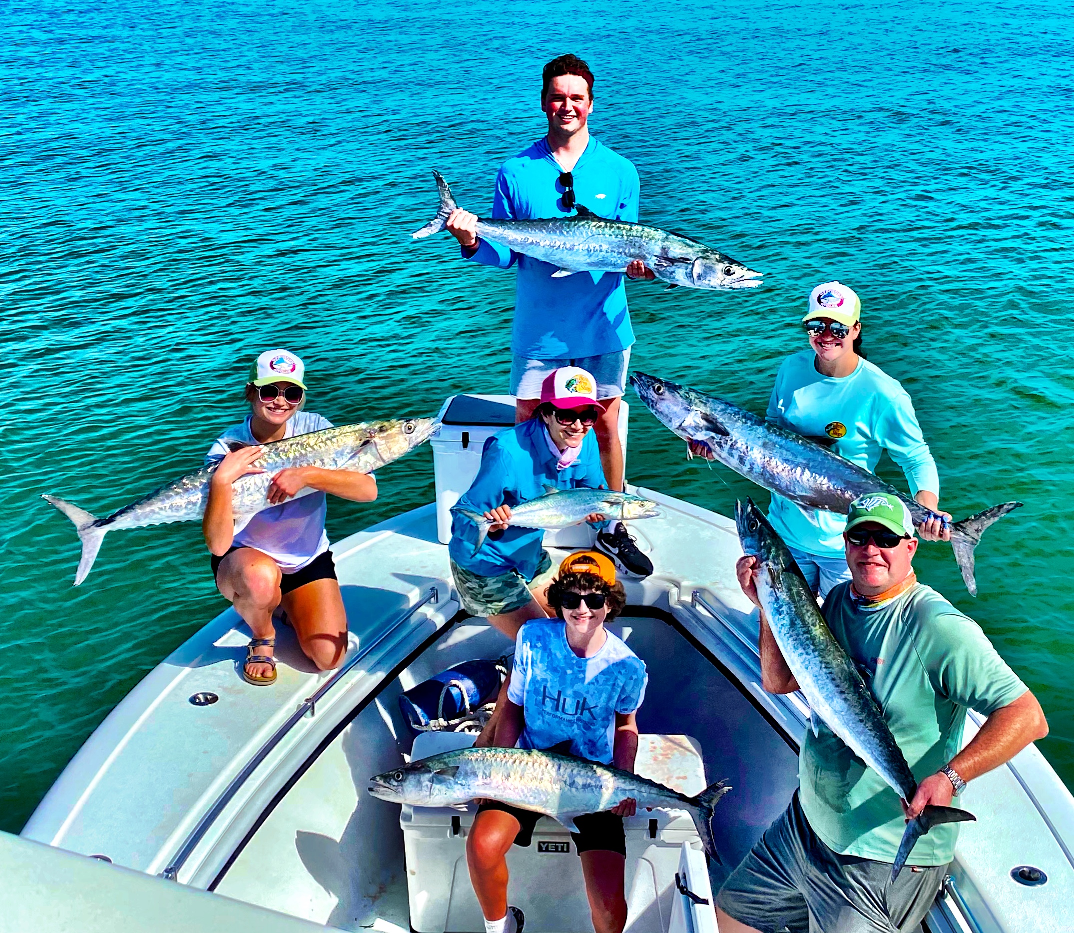 Group of anglers on a boat in the Gulf of Mexico, proudly displaying their catch of Kingfish, with clear blue water in the background, showcasing a successful Gulf wreck fishing trip.