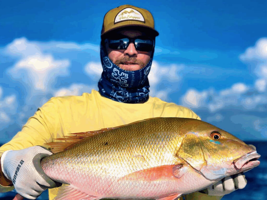Man holding a Mutton Snapper, showcasing vibrant colors against a blue sky, highlighting successful reef fishing in the Florida Keys.