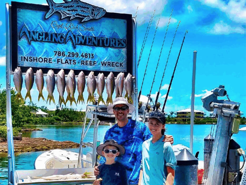 Family fishing trip in the Florida Keys with a man and two children proudly displaying a catch of Yellowtail Snapper on a charter boat, featuring fishing rods and a scenic waterfront backdrop.